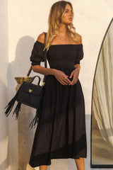 Woman wearing black off-shoulder bohemian maxi dress with flowing skirt and puff sleeves.