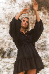 Model wearing black bohemian mini dress with flowing sleeves and relaxed silhouette.